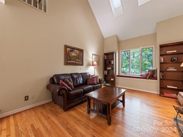 living room featuring a skylight, high vaulted ceiling, and light hardwood / wood-style floors