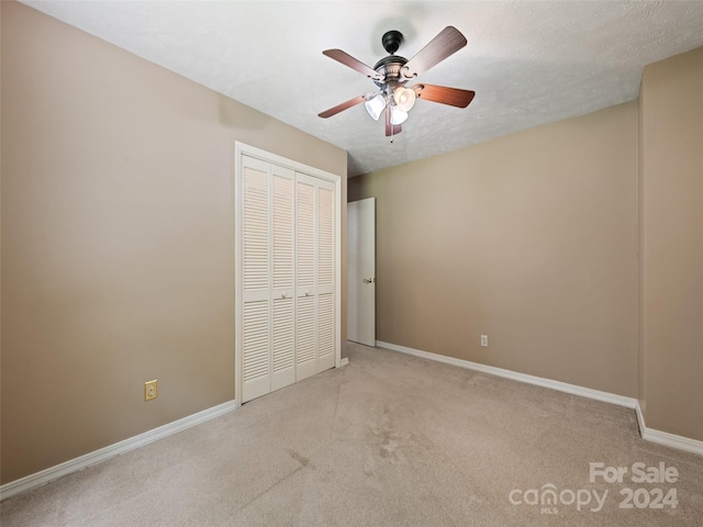 unfurnished bedroom with ceiling fan, a closet, light colored carpet, and a textured ceiling