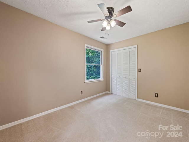 unfurnished bedroom featuring ceiling fan, a closet, light colored carpet, and a textured ceiling