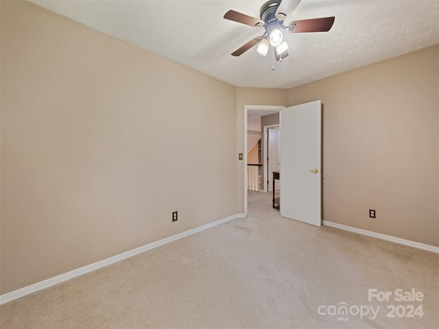 empty room with ceiling fan, light colored carpet, and a textured ceiling