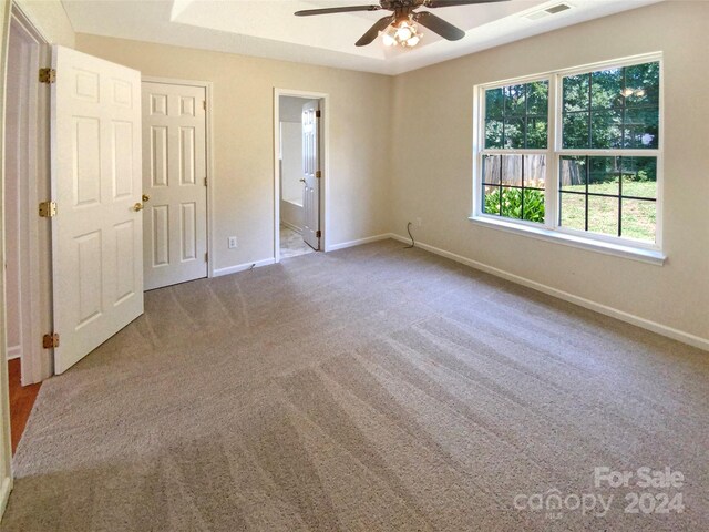 unfurnished bedroom featuring a raised ceiling, ceiling fan, carpet, and connected bathroom