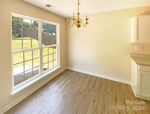 unfurnished dining area with a notable chandelier, a textured ceiling, and light hardwood / wood-style flooring