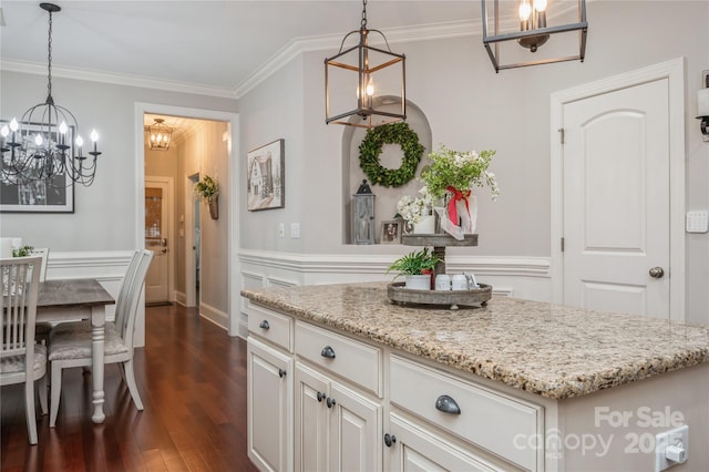 kitchen featuring light stone counters, white cabinets, decorative light fixtures, and ornamental molding