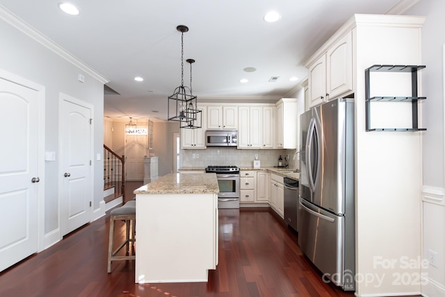 kitchen featuring light stone counters, stainless steel appliances, crown molding, decorative light fixtures, and a kitchen island