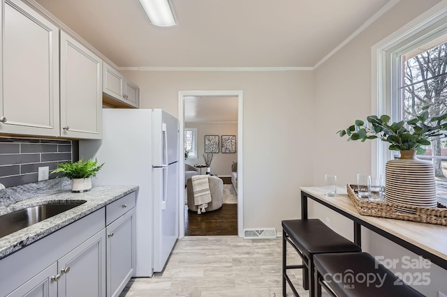 kitchen with visible vents, decorative backsplash, light stone counters, crown molding, and a sink