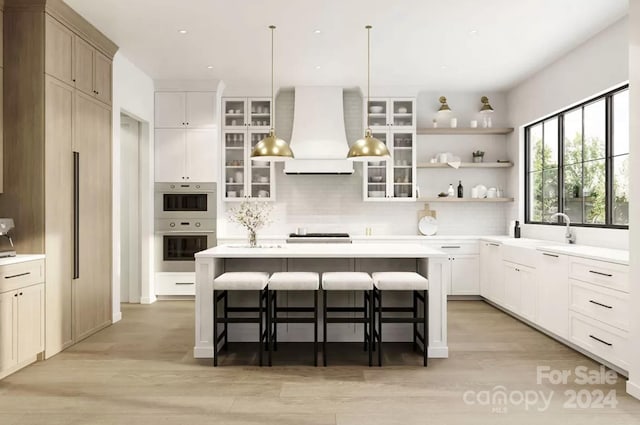 kitchen featuring white cabinetry, hanging light fixtures, a breakfast bar area, a kitchen island with sink, and exhaust hood