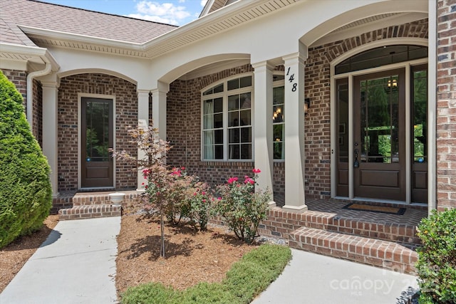 entrance to property with covered porch, roof with shingles, and brick siding