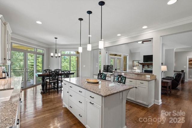 kitchen featuring white cabinets, a kitchen island, ornamental molding, dark wood-type flooring, and a fireplace