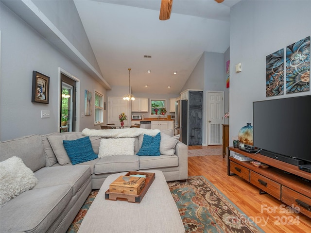 living room with high vaulted ceiling, ceiling fan with notable chandelier, and light hardwood / wood-style flooring