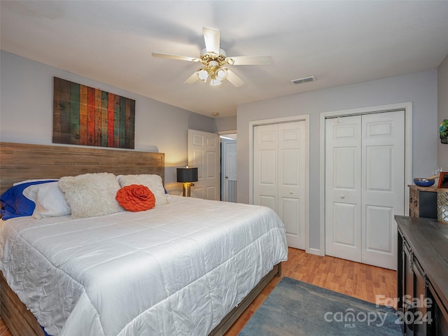 bedroom with ceiling fan, two closets, and hardwood / wood-style floors