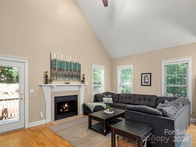 living room featuring hardwood / wood-style flooring, ceiling fan, high vaulted ceiling, and a tiled fireplace