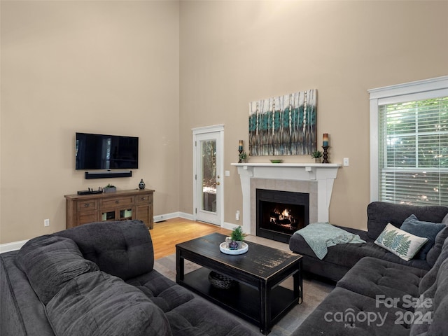 living room with a tiled fireplace, a towering ceiling, and wood-type flooring