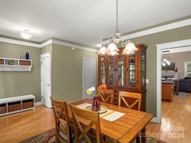 dining space with light wood-type flooring, a notable chandelier, and ornamental molding