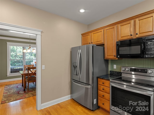 kitchen featuring dark stone counters, light hardwood / wood-style floors, appliances with stainless steel finishes, and an inviting chandelier