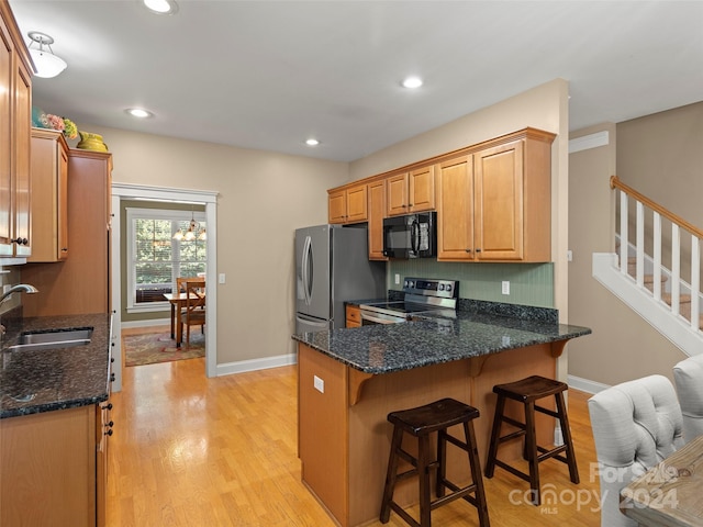 kitchen with sink, stainless steel appliances, kitchen peninsula, dark stone countertops, and light hardwood / wood-style floors