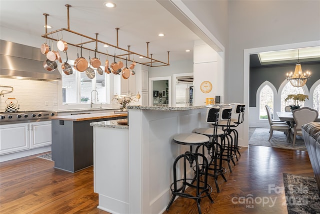 kitchen with light stone countertops, white cabinets, ventilation hood, and stainless steel gas cooktop