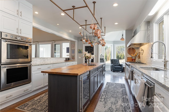 kitchen with white cabinets, wooden counters, a kitchen island, stainless steel appliances, and sink