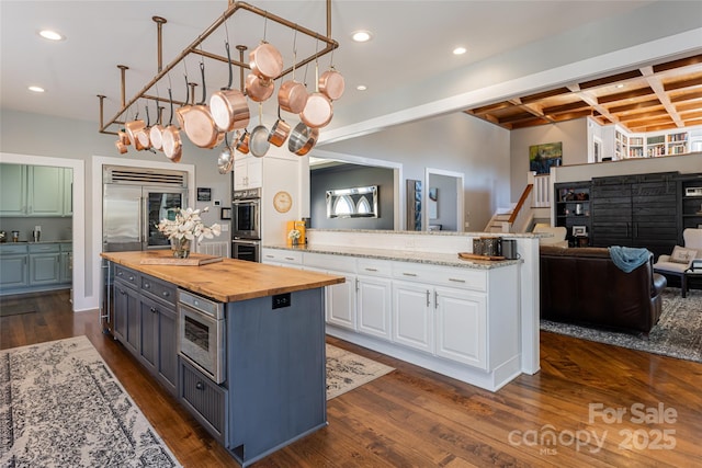 kitchen with a center island, beamed ceiling, built in appliances, white cabinetry, and wood counters