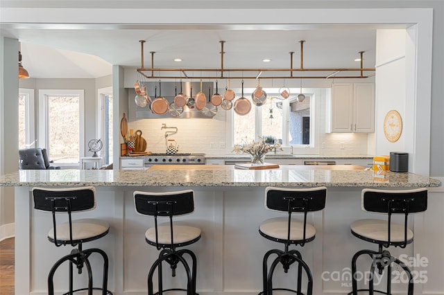 kitchen with a kitchen bar, white cabinetry, backsplash, light stone counters, and stove