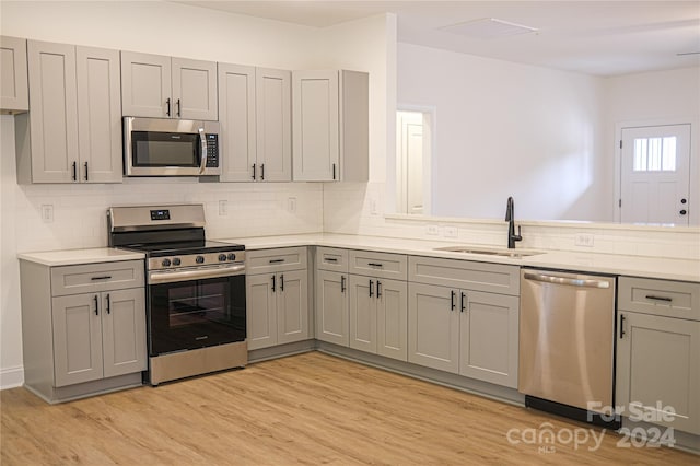 kitchen featuring backsplash, gray cabinets, sink, light hardwood / wood-style flooring, and appliances with stainless steel finishes