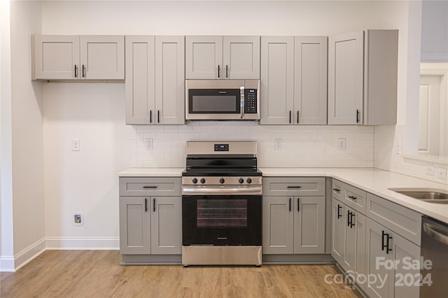 kitchen featuring light hardwood / wood-style floors, decorative backsplash, gray cabinets, and stainless steel appliances