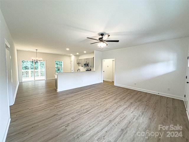 unfurnished living room featuring hardwood / wood-style flooring and ceiling fan with notable chandelier