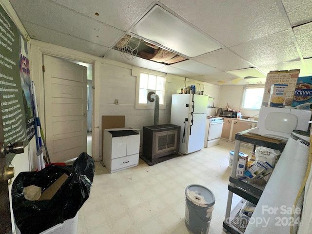 kitchen with a paneled ceiling, a wood stove, and white appliances