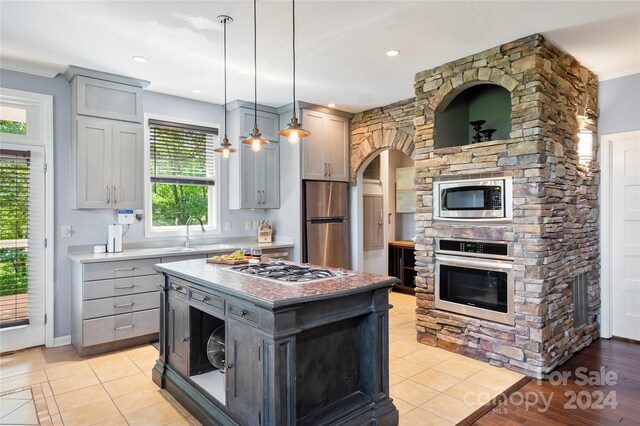 kitchen with pendant lighting, a center island, stainless steel appliances, light tile patterned floors, and gray cabinetry