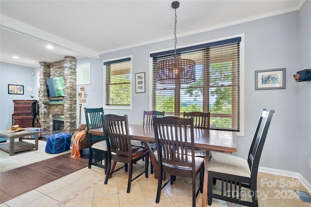 dining room with light tile patterned floors, a stone fireplace, visible vents, baseboards, and ornamental molding