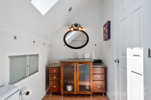 bathroom featuring vanity, lofted ceiling with skylight, tile patterned flooring, and toilet