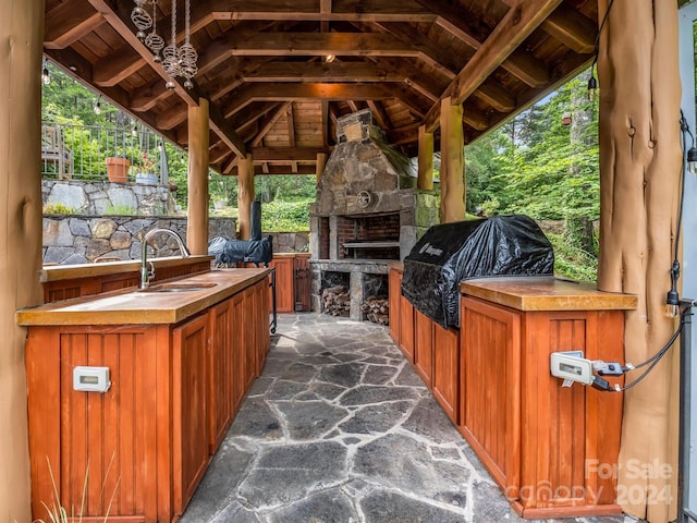 view of patio with a gazebo, area for grilling, sink, and an outdoor stone fireplace