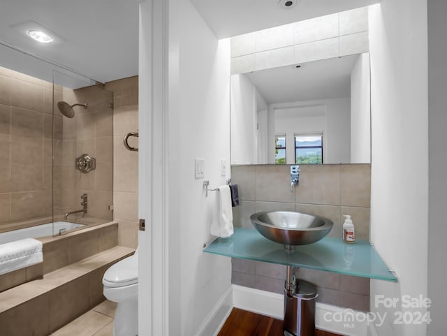 full bathroom with tiled shower / bath combo, toilet, sink, and tasteful backsplash