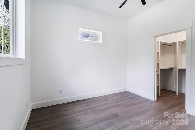 unfurnished bedroom featuring a walk in closet, a closet, dark wood-type flooring, a ceiling fan, and baseboards