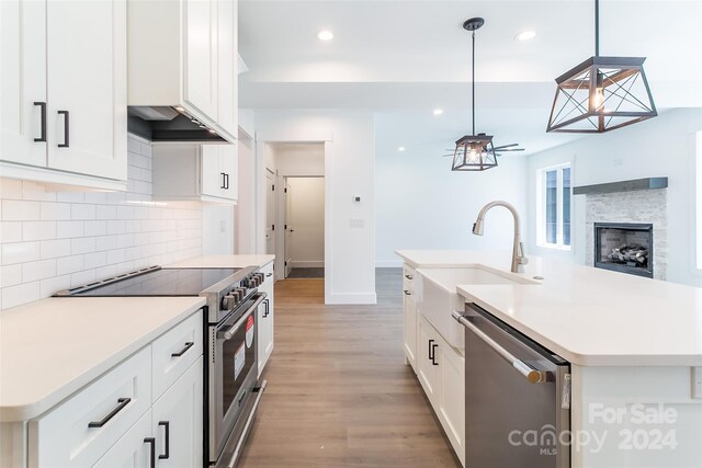 kitchen featuring pendant lighting, white cabinets, stainless steel appliances, an island with sink, and sink