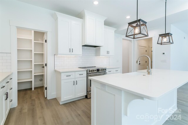 kitchen with a kitchen island with sink, light wood-type flooring, hanging light fixtures, stainless steel electric range, and white cabinets