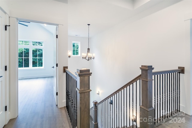 hall with light hardwood / wood-style floors, lofted ceiling, and a notable chandelier