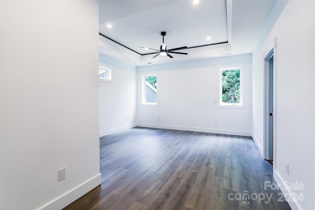 empty room featuring dark wood-style flooring, recessed lighting, a raised ceiling, and baseboards