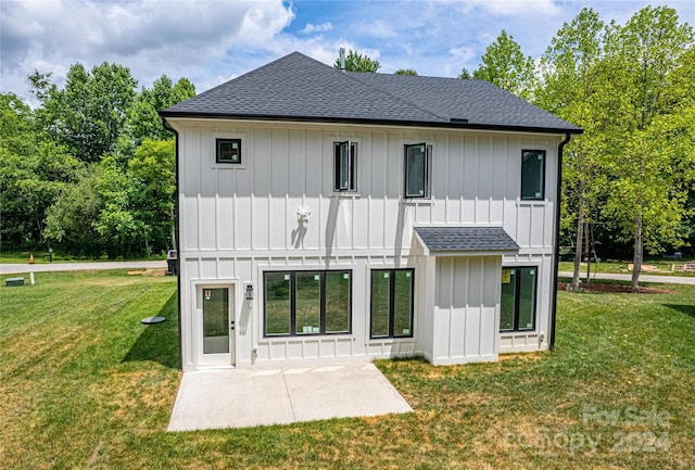 rear view of house with a patio area, a shingled roof, a lawn, and board and batten siding