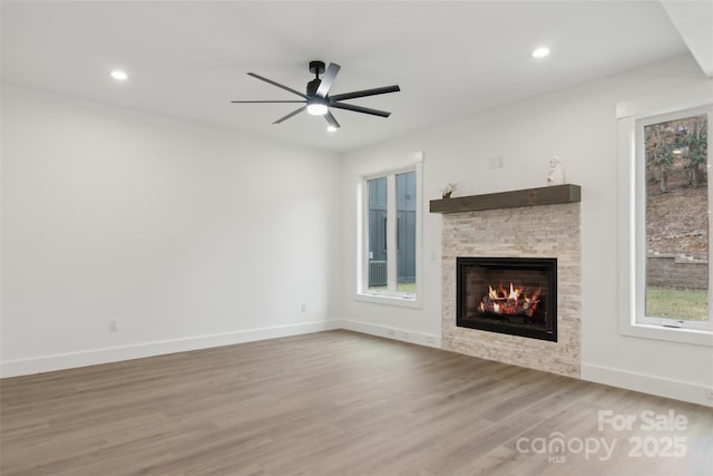 unfurnished living room featuring wood finished floors, baseboards, a ceiling fan, recessed lighting, and a stone fireplace