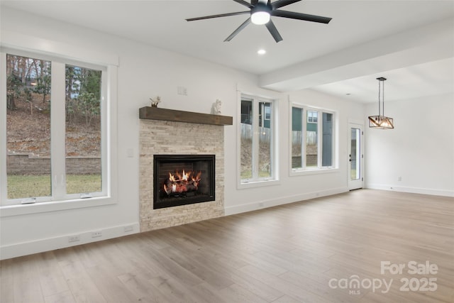 unfurnished living room featuring a wealth of natural light, baseboards, a stone fireplace, and wood finished floors