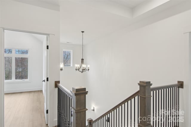 hallway with wood finished floors, an upstairs landing, baseboards, and a chandelier
