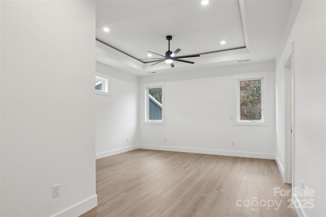 unfurnished room with a raised ceiling, light wood-style flooring, and baseboards