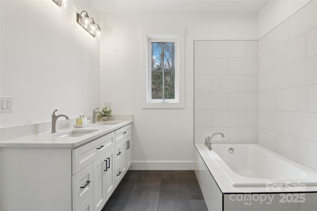 bathroom with double vanity, a bath, baseboards, and a sink