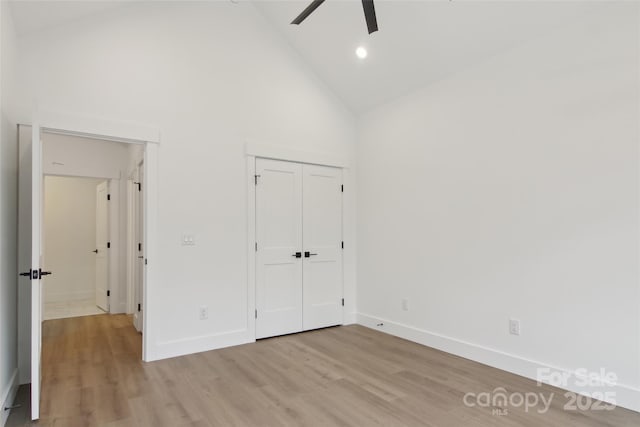unfurnished bedroom with light wood-type flooring, high vaulted ceiling, a closet, baseboards, and ceiling fan