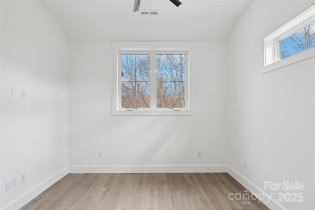 spare room featuring vaulted ceiling, visible vents, baseboards, and wood finished floors