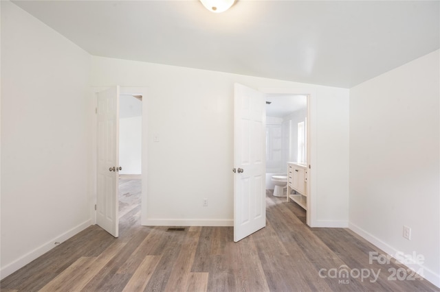 unfurnished bedroom featuring ensuite bath, vaulted ceiling, and hardwood / wood-style flooring