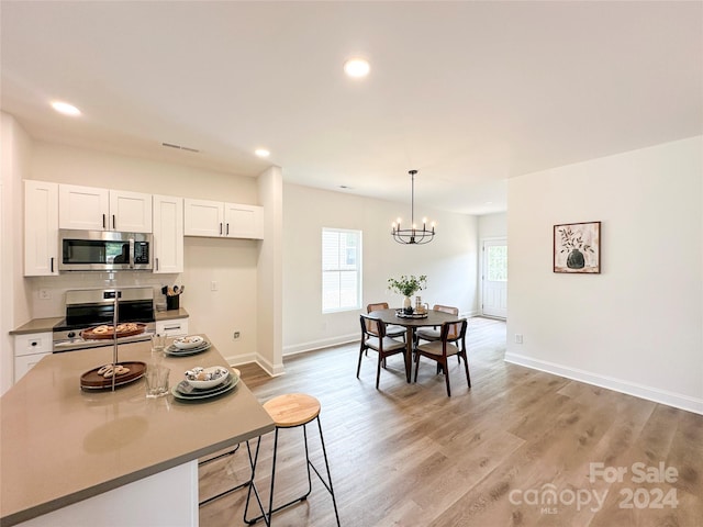 kitchen with appliances with stainless steel finishes, pendant lighting, white cabinets, a notable chandelier, and light hardwood / wood-style flooring