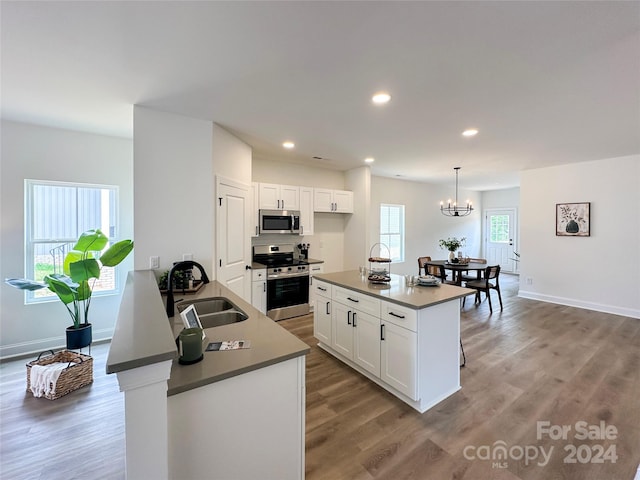 kitchen with stainless steel appliances, white cabinetry, sink, and decorative light fixtures