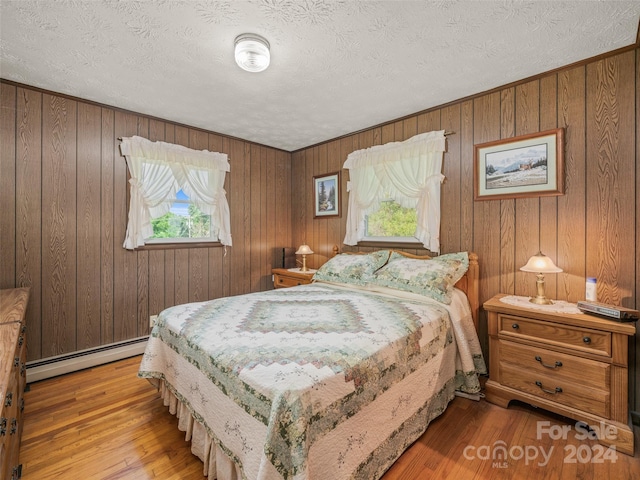 bedroom with baseboard heating, wood-type flooring, and a textured ceiling