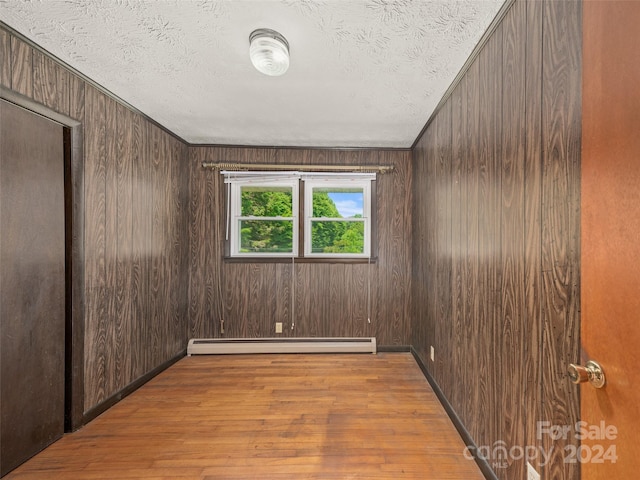 unfurnished room with baseboard heating, light hardwood / wood-style flooring, and wood walls